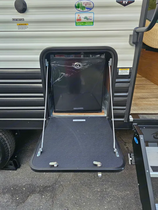 An RV rental's side, featuring an open outdoor compartment with a new, wrapped mini-fridge. Safety notices visible on the camper.. Forest River Wolf pup 17JW 2023