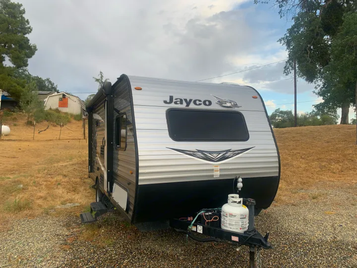 A gray and black Jayco RV rental travel trailer sits on a gravel lot under a cloudy sky.. Jayco Jay Flight SLX 2020