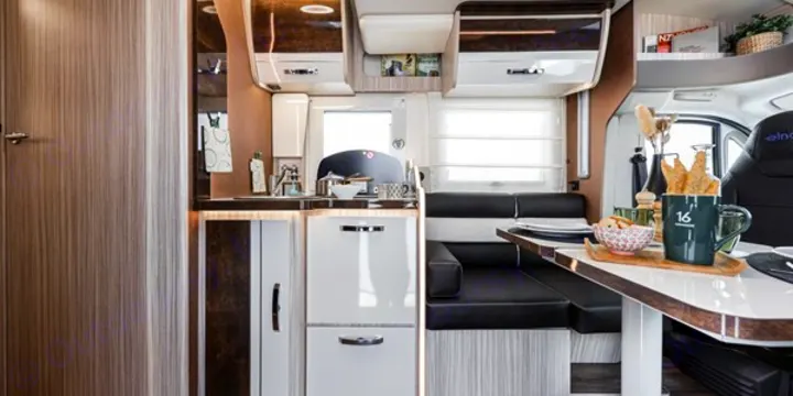 Explore this RV rental's interior: a stylish compact kitchen with integrated fridge, and a comfortable dinette with black seating.. Elnagh 582 2023