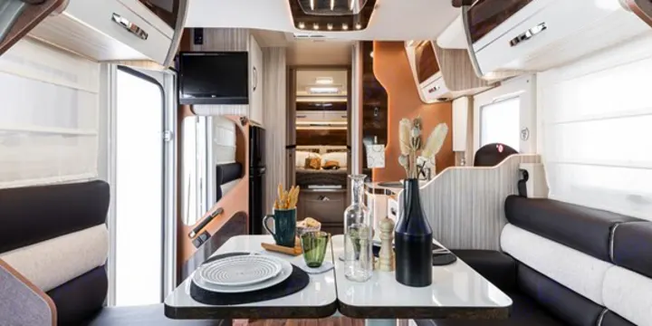 Inside a stylish RV rental: a bright dining & living area with a TV, leading to a cozy rear bedroom.. Elnagh 582 2023