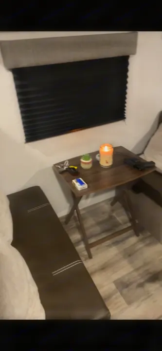 RV rental interior featuring a comfy bench and window. A small table holds a lit candle, keys, cigarettes, and a handgun.. Coleman Lantern 17B 2023