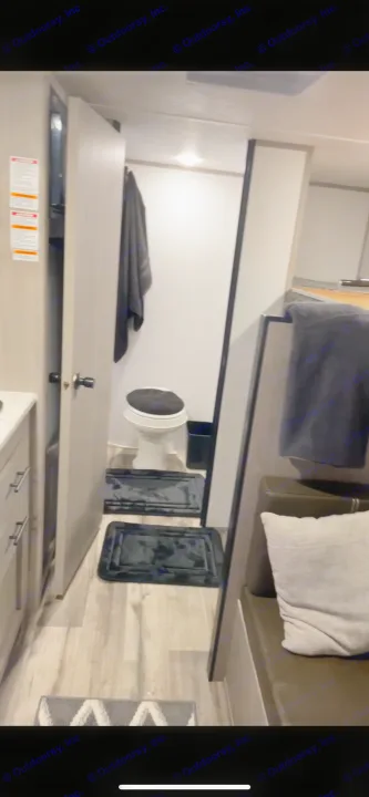 Inside an RV rental: a compact bathroom with black mats, an open door, and a cozy seating area.. Coleman Lantern 17B 2023