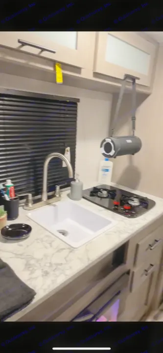 Compact RV rental kitchen with a sink, two-burner stove, marble countertop, and overhead cabinets.. Coleman Lantern 17B 2023