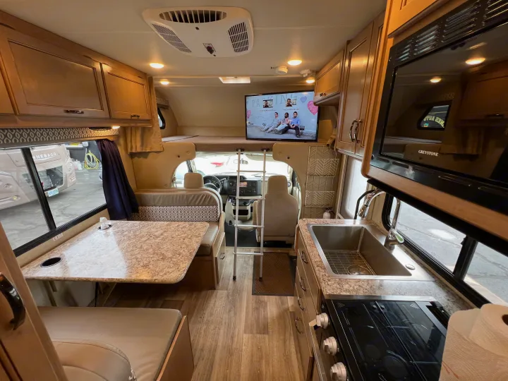 Clean rv rental interior: dinette, full kitchen, overhead bunk with TV, and driving cabin. Ready for adventure!. Thor Motor Coach Freedom Elite 2019
