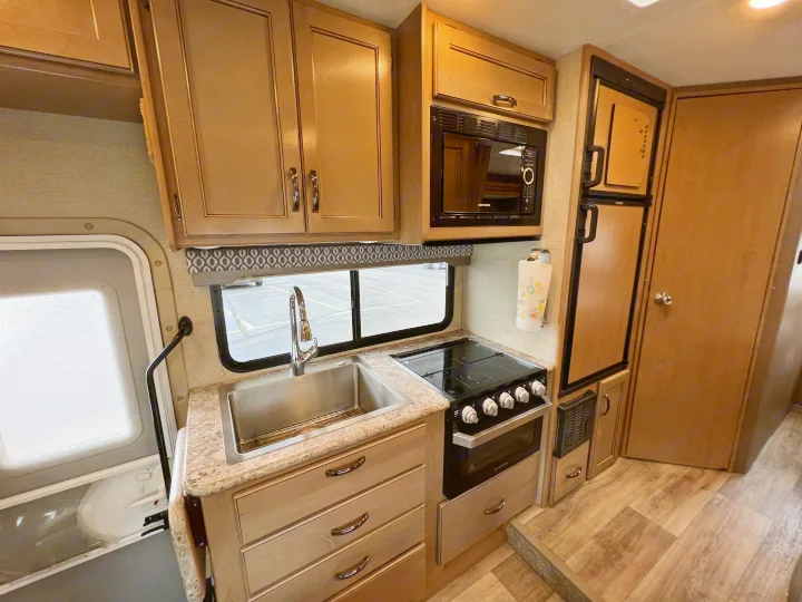 RV rental kitchen: light wood cabinets, stainless sink, stovetop, oven, microwave, and refrigerator.. Thor Motor Coach Freedom Elite 2019
