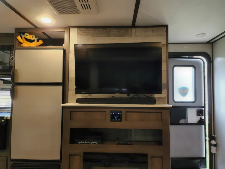 Inside this RV rental: a living area with TV, soundbar, media console, Dometic fridge, and an exit door.. Dutchmen Coleman Light 2021