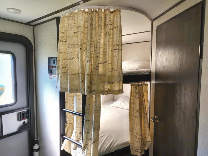 Inside an RV rental: bunk beds with script curtains, a control panel, and an entry door.. Dutchmen Coleman Light 2021