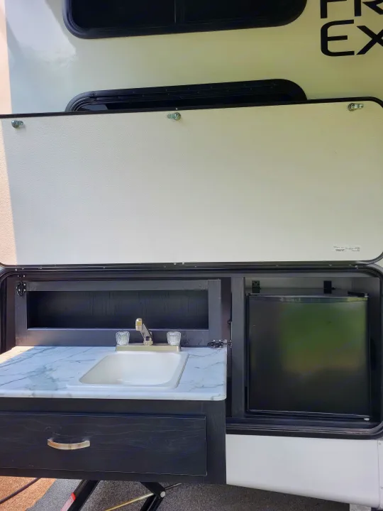 RV rental: Convenient outdoor kitchen in an open compartment, featuring a sink, faucet, mini-fridge, and storage. Ideal for camping.. Coachmen Freedom Express Ultra Lite 257BHS 2023