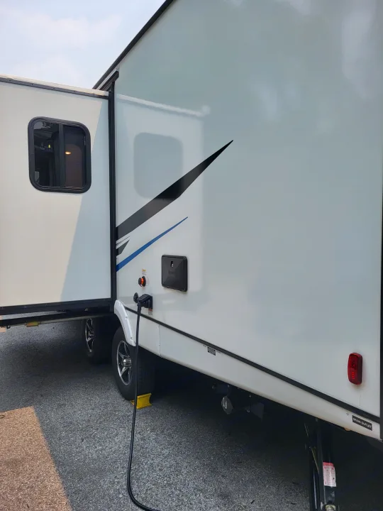This RV rental shows its side with the slide-out extended, power cord connected, and exterior utility access.. Coachmen Freedom Express Ultra Lite 257BHS 2023