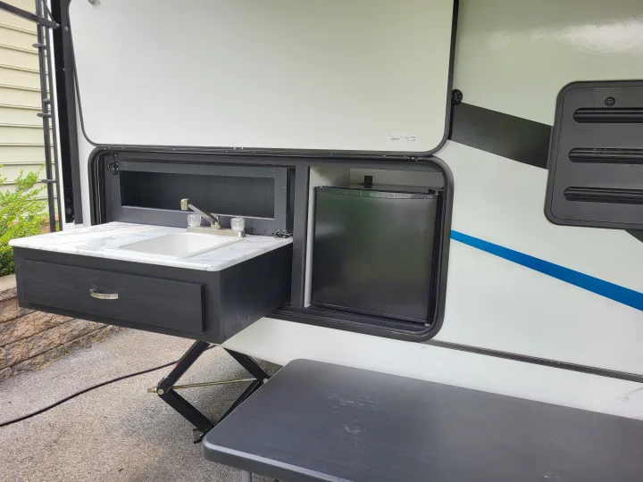 This RV rental boasts an outdoor kitchen with a sink, mini-fridge, and counter, enhancing your camping experience.. Coachmen Freedom Express Ultra Lite 257BHS 2023