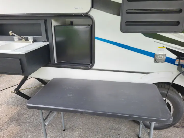 RV rental's outdoor kitchen with sink, mini-fridge, and a portable table for convenient camping setup.. Coachmen Freedom Express Ultra Lite 257BHS 2023