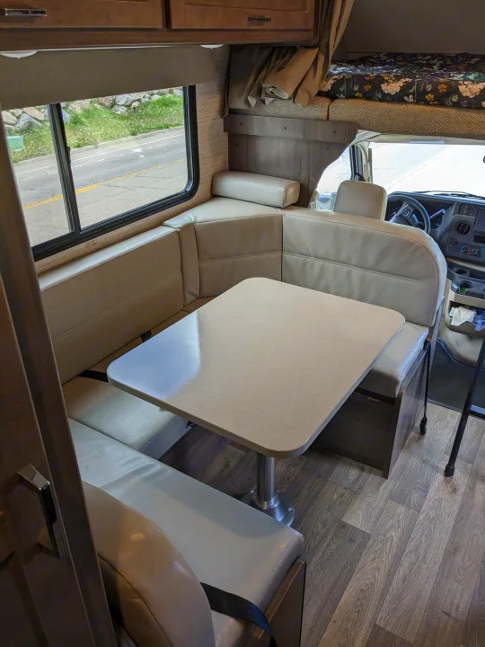 Inside this RV rental: A light dinette with banquette seating, table, wood-look floor, and overhead bunk for comfort.. Winnebago Minnie Winnie 2022