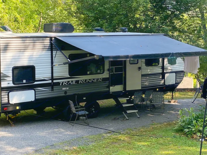 A Trail Runner RV rental with extended awning, chairs, and clothes drying, parked at a sunny campsite.. Heartland Trail Runner 2022