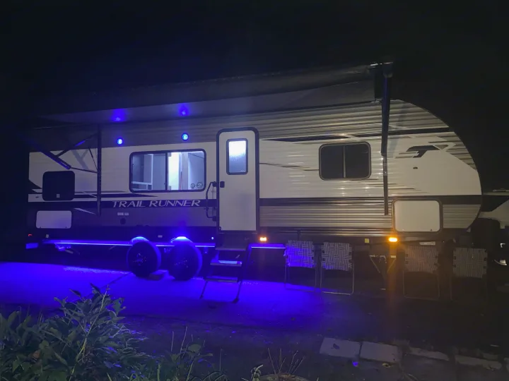 This RV rental, a "TRAIL RUNNER" travel trailer, illuminates the night with vibrant blue underglow and awning lights.. Heartland Trail Runner 2022