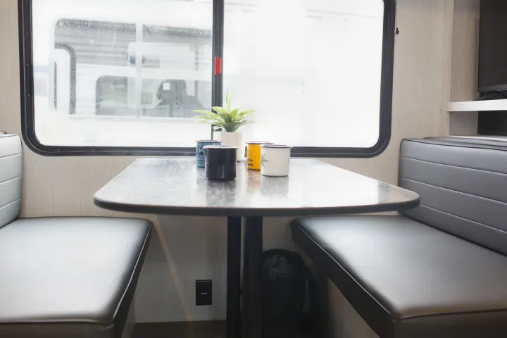 RV rental interior: Comfortable dining booth with table, plant, mugs, and a bright window view.. Heartland Trail Runner 2022