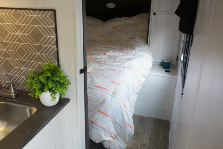 Inside a comfy RV rental: a bright patterned bed in a sleeping nook & compact kitchen counter with sink.. Heartland Trail Runner 2022