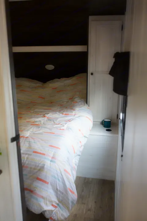Cozy RV rental bedroom: colorful patterned bed, dark headboard, light cabinet, teal mug. A comfortable, well-appointed interior space.. Heartland Trail Runner 2022