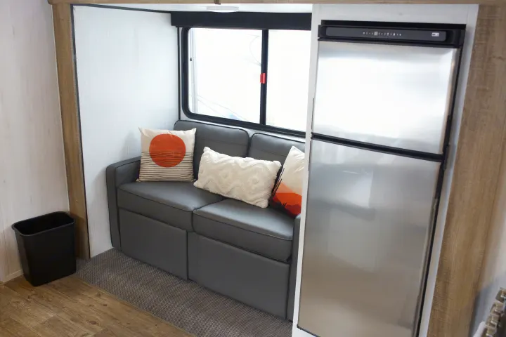 Cozy RV rental interior: dark grey sofa with decorative pillows, large window, and silver refrigerator unit.. Heartland Trail Runner 2022