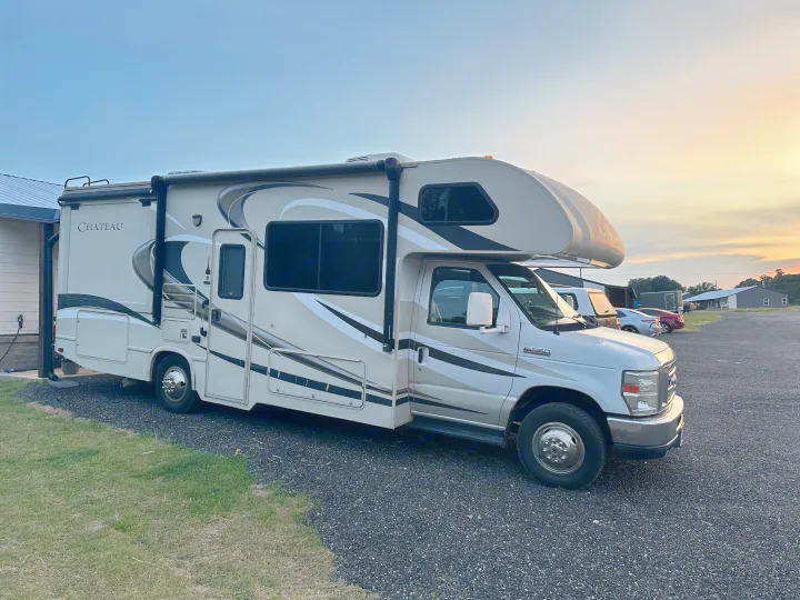 A light-colored Chateau Class C RV rental, plugged in and parked on a gravel lot at sunset. Perfect for your next travel adventure.. Thor Chateau 2015