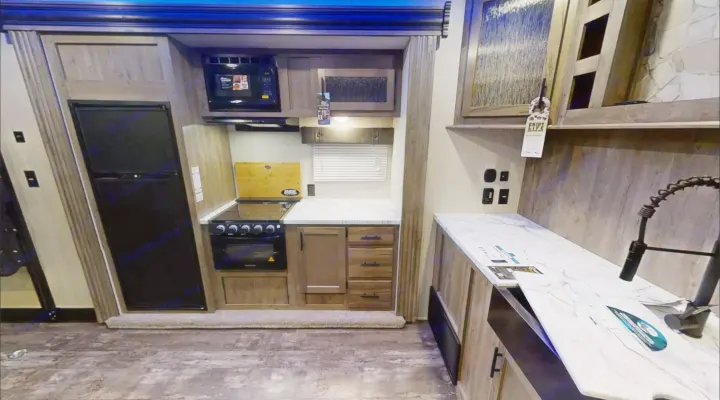 This modern RV rental kitchen features a fridge, stove, microwave, sink, and stylish marble-look countertops for comfortable travel.. Forest River Cherokee Wolf Pack 2020