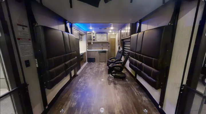 Spacious RV rental toy hauler interior, featuring a kitchen, lounge chairs, and versatile wall-mounted seating/beds.. Forest River Cherokee Wolf Pack 2020