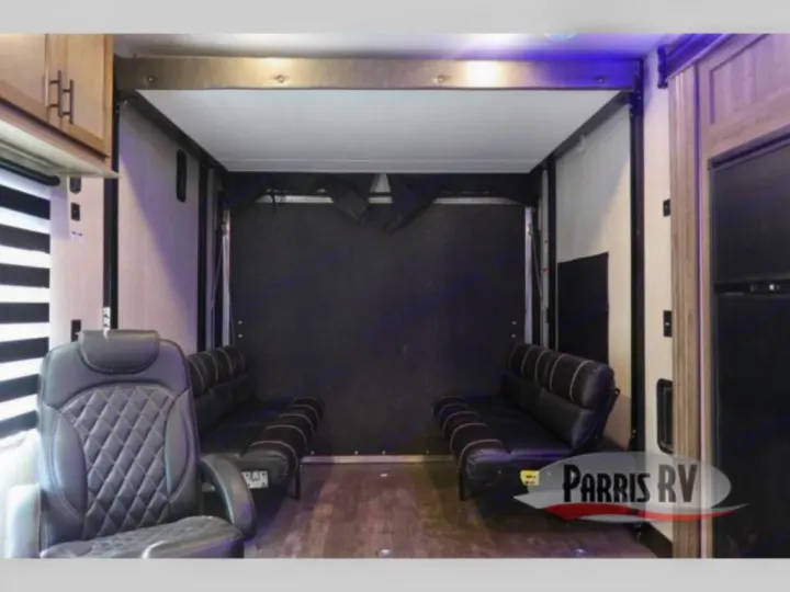 RV rental toy hauler interior: versatile garage space with black fold-down sofas, an armchair, & wood-look floor.. Forest River Cherokee Wolf Pack 2020