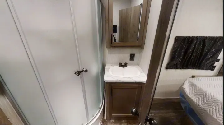 Compact RV rental bathroom featuring a frosted glass shower, vanity with sink, mirror, and a glimpse of the adjacent bedroom. Ideal for travel.. Forest River Cherokee Wolf Pack 2020