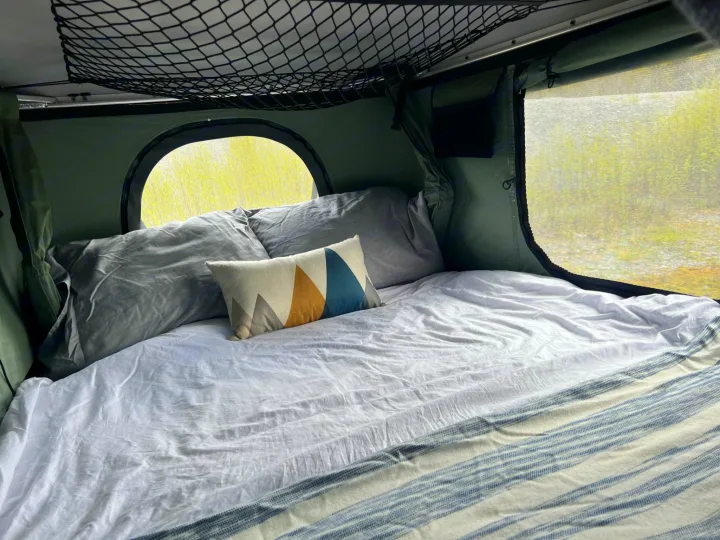 Cozy RV rental interior: a comfy bed with pillows, round window, & mesh screen for serene outdoor views.. Toyota Tacoma 2012