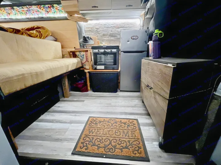 Cozy RV rental interior showcasing a compact kitchen, refrigerator, sofa, and wood flooring. Ideal for comfortable mobile living.. Dodge Ram ProMaster 2500 High Top 2018