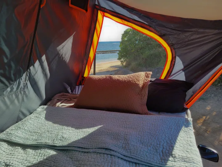 Inside a cozy RV rental, a bed with soft green bedding faces a scenic window offering panoramic views of a sunny beach and ocean.. Nissan Exterra 2011