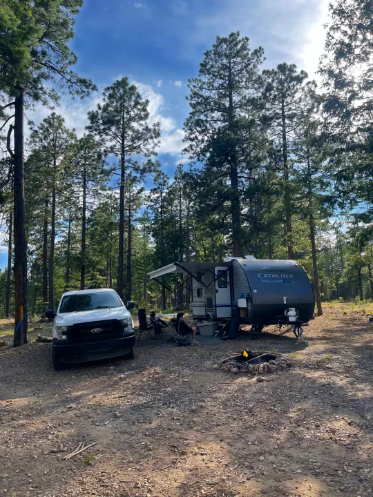 Experience forest camping! This RV rental, a Coachmen Catalina travel trailer, is set up with a truck amidst tall pine trees.. Coachmen Catalina Summit 2022