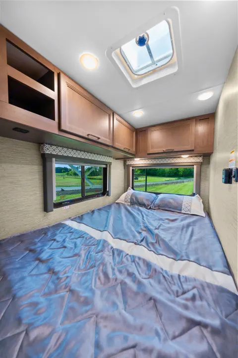 Cozy RV rental bedroom featuring a spacious bed, ample storage cabinets, bright windows, and an overhead skylight.. Thor Coleman 2023