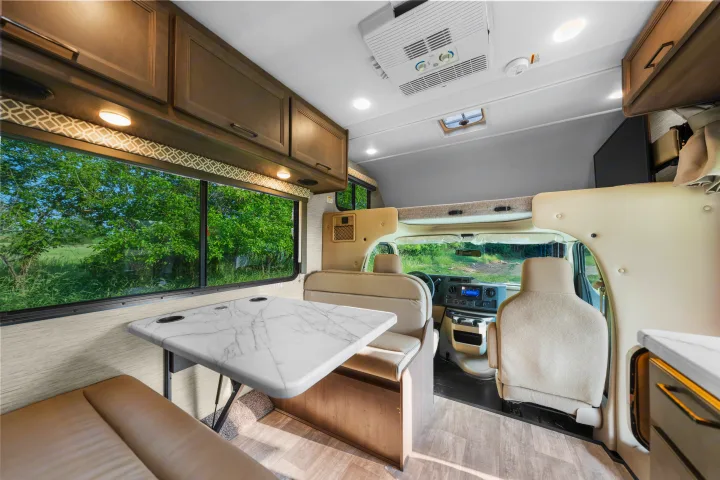 Spacious RV rental interior with a modern dining area, large scenic windows, and front cockpit with an overhead bunk.. Thor Coleman 2023