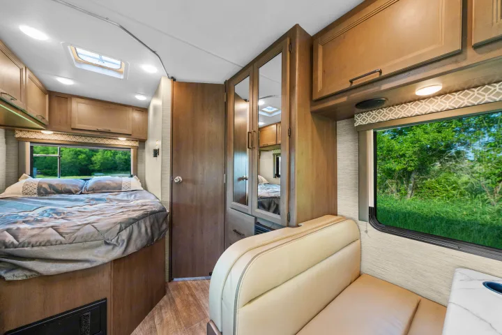 Spacious RV rental interior with a cozy bed, bright windows, comfortable dinette seating, and ample storage for travel.. Thor Coleman 2023
