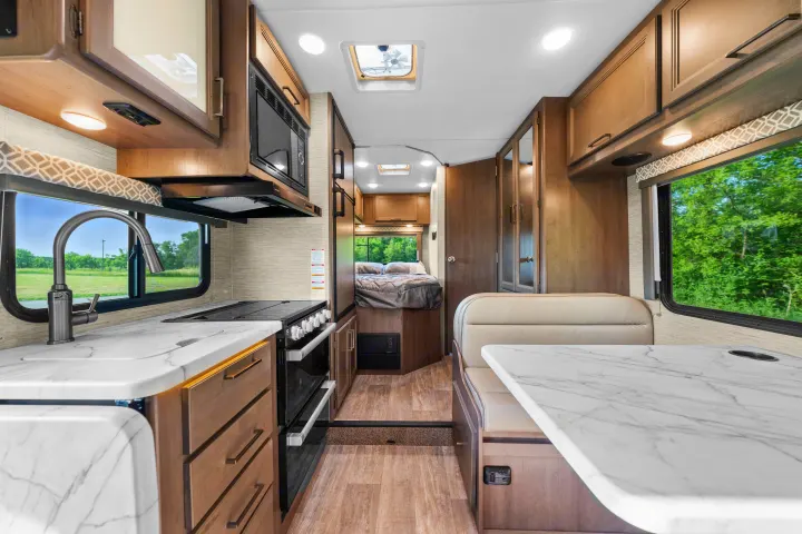 Modern RV rental interior: view from front shows kitchen, dining booth, and rear bed. Bright, clean mobile living space.. Thor Coleman 2023