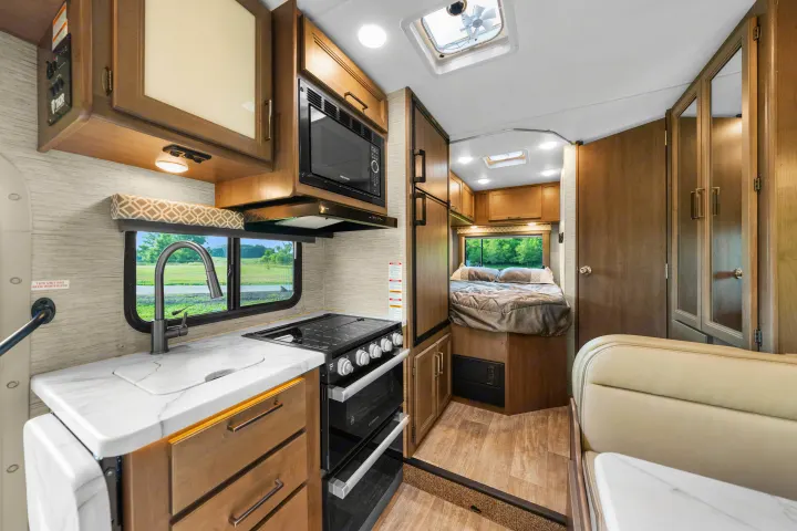 Inside a comfortable RV rental: full kitchen with microwave & stove, dinette, and a cozy bedroom.. Thor Coleman 2023