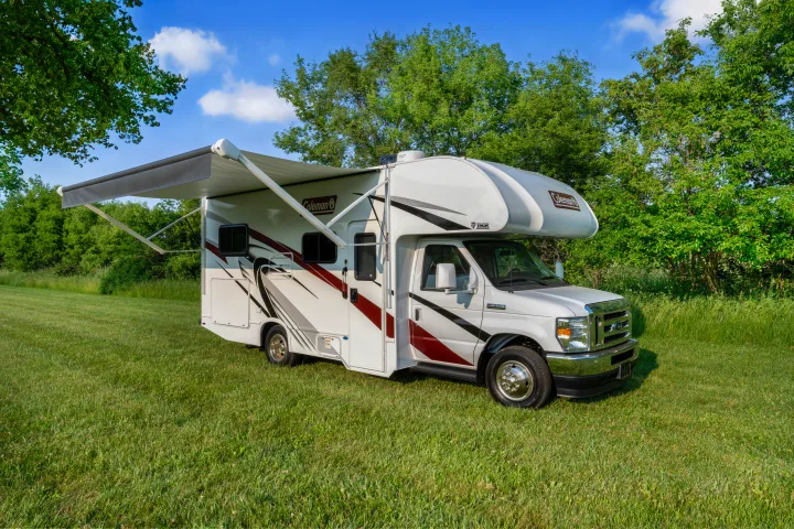 Spacious Coleman RV rental with extended awning parked in a sunny grassy field, perfect for your next camping trip.. Thor Coleman 2023