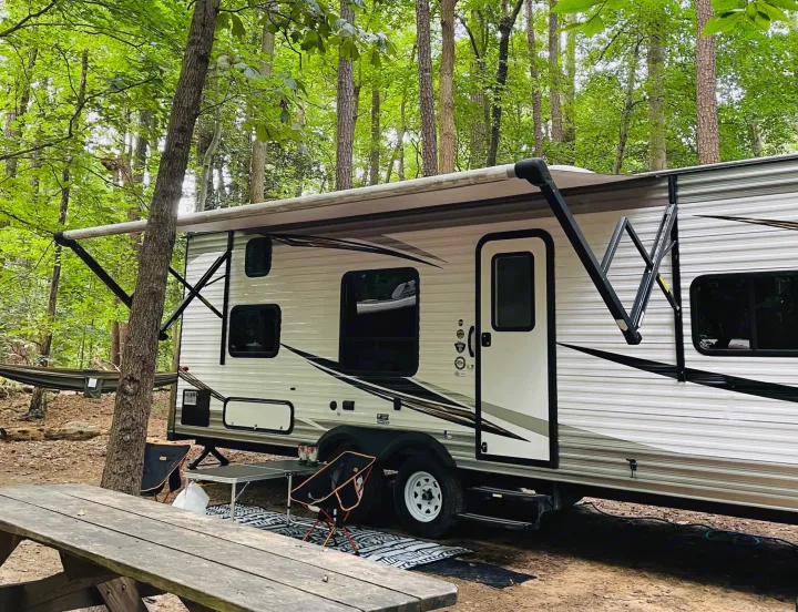 RV rental parked in a tranquil wooded campsite, featuring an extended awning, picnic table, and hammock.. Jayco Jay Flight SLX 2019