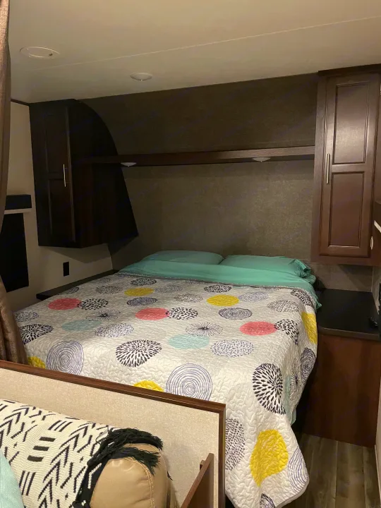 Cozy RV rental bedroom with a colorful patterned quilt on the bed, mint sheets, and dark wood cabinets.. Jayco Jay Flight SLX 2019
