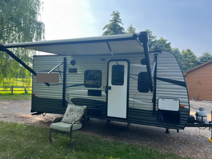 This RV rental travel trailer with an extended awning is parked outside with a chair, ready for your next adventure.. Keystone RV Summerland Mini 2017