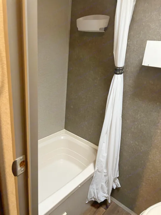 Compact RV rental bathroom: white shower/tub, tied-back shower curtain. A practical interior for travel.. Keystone RV Summerland Mini 2017
