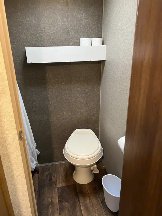 RV rental bathroom: a clean, compact space with toilet, a small shelf holding toilet paper, and wood-look flooring.. Keystone RV Summerland Mini 2017