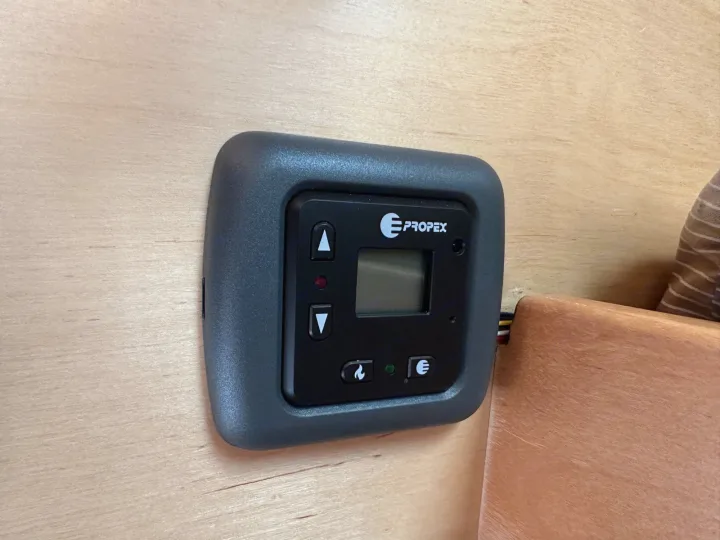 A black Propex climate control panel with display and buttons, mounted on light wood in an RV rental.. Little Guy Little Guy Trailer 2013