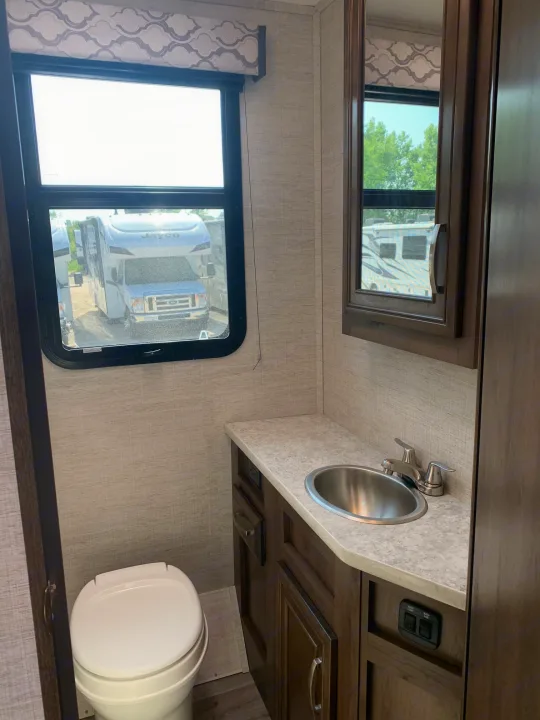 Compact RV rental bathroom showcasing a sink, toilet, vanity, mirror, and two windows providing outdoor views.. Jayco Redhawk 29XK 2023