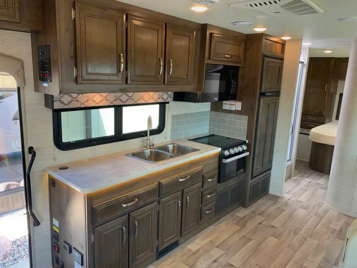 Step into this modern RV rental kitchen! Featuring sleek wood cabinets, light counters, double sink, stove, microwave, and fridge.. Jayco Redhawk 29XK 2023
