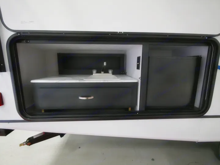 This RV rental showcases an outdoor kitchen: a marble-look counter with sink and faucet, plus a mini-fridge.. Coachmen 257BHS 2022