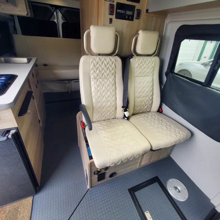 View of a comfortable RV rental interior with beige quilted seats, a compact kitchen counter, and control panel. Textured floor.. Winnebago Solis 2022