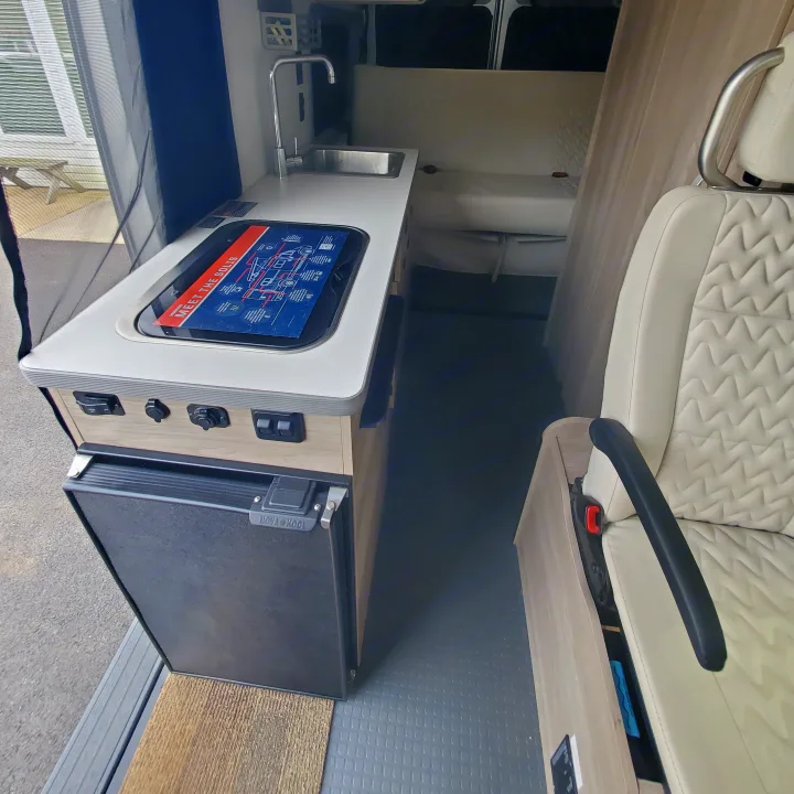Explore this modern RV rental interior featuring a compact kitchen, sink, fridge, and quilted seating. Perfect for adventure.. Winnebago Solis 2022