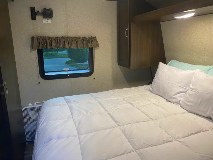 Inside an RV rental: a comfortable bedroom featuring a queen bed, window, and storage cabinets. Ready for your adventure.. Keystone RV Hideout 2023