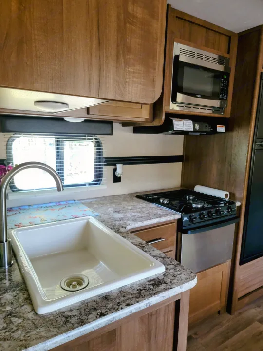 Clean rv rental kitchen featuring a light-colored sink, stainless steel microwave/stove, and rich wood cabinets.. Aspen Trail Aspen Trail Trailer 2018